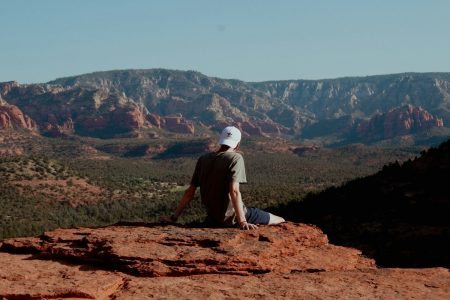 Man sitting on a red rock ledge looking out over the Sedona valley